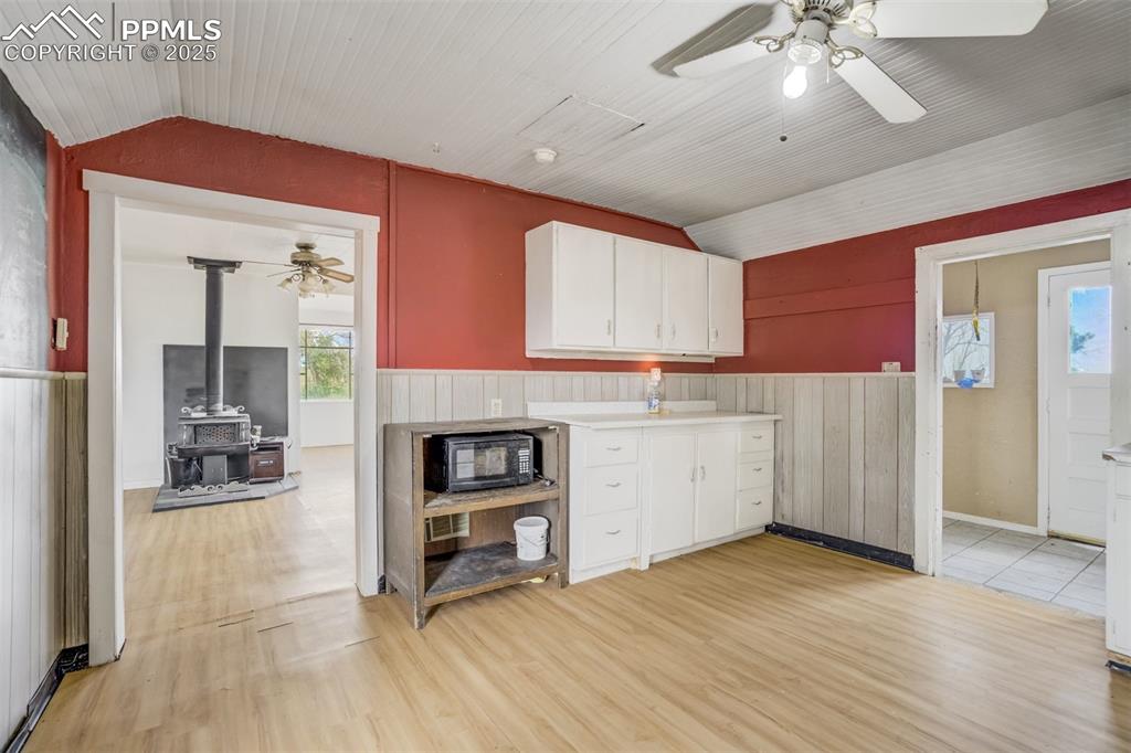 Image 37 of 50: Kitchen featuring vaulted ceiling, a ceiling fan, a wood stove, light wood-