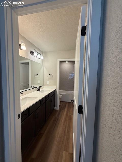 Image 10 of 11: Full bath featuring wood finished floors, a textured ceiling, double vanity