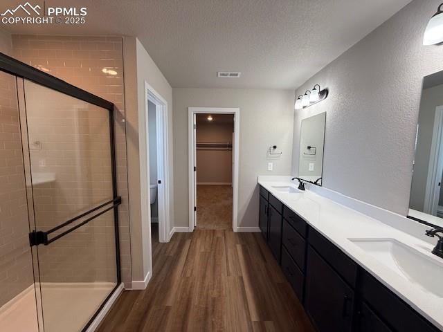 Image 3 of 11: Full bath with double vanity, wood finished floors, a shower stall, a textu