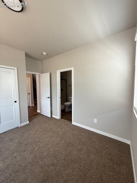 Image 6 of 11: Unfurnished bedroom featuring dark carpet, connected bathroom, and a textur
