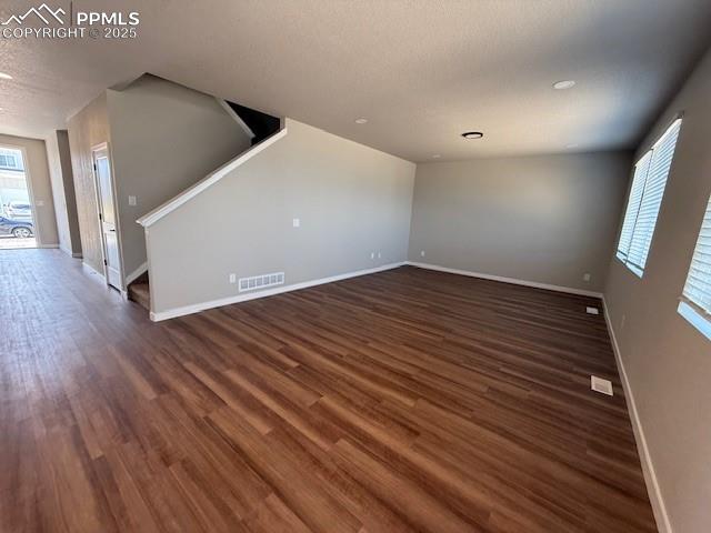 Image 8 of 11: Unfurnished living room with a textured ceiling, dark wood-style flooring,
