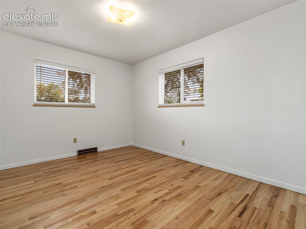 Image 13 of 34: Two windows with blinds, wood-finish flooring, and a ceiling-mounted light