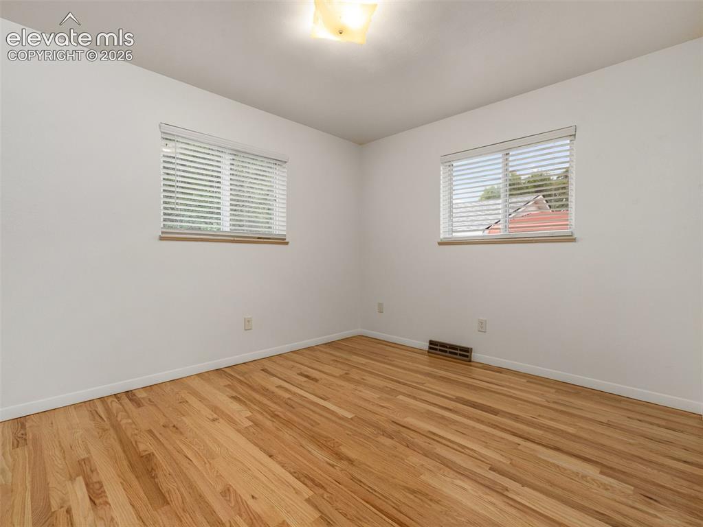 Image 16 of 34: Hardwood flooring throughout, two windows with blinds, and flush-mount ligh