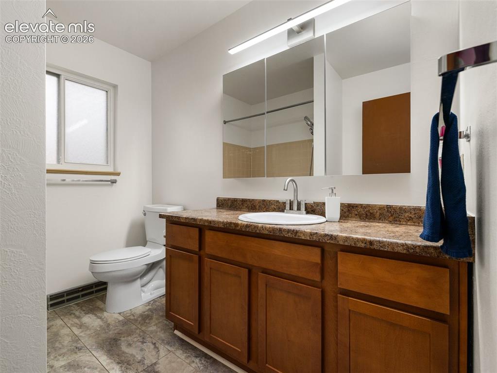 Image 18 of 34: Single vanity with wood-finish cabinetry, integrated sink, and composite co