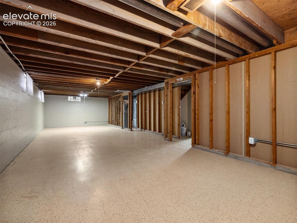 Image 24 of 34: Spacious unfinished lower level with exposed wood joists and concrete block