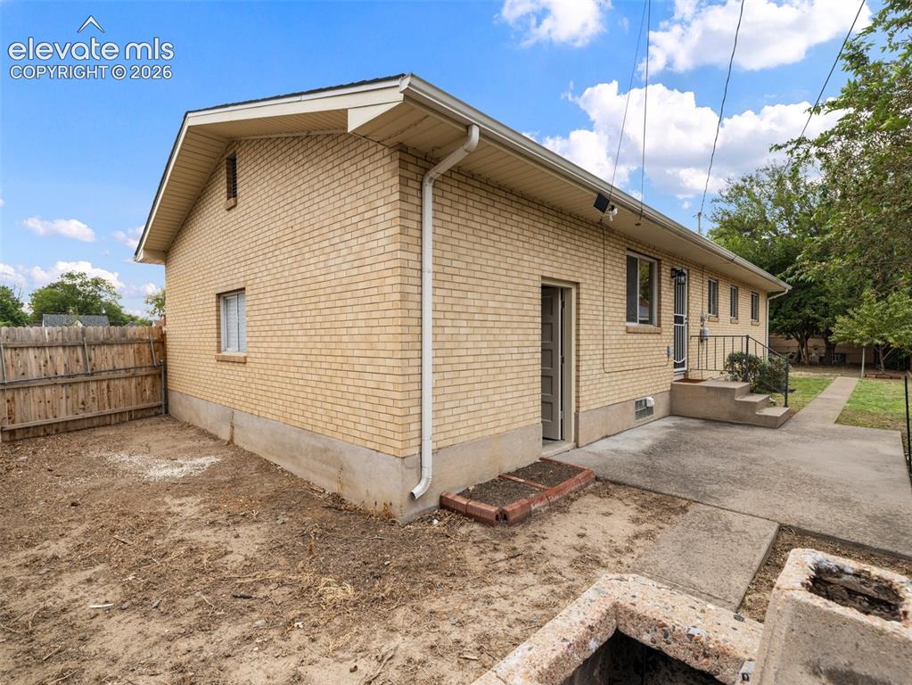 Image 26 of 34: Brick exterior with multiple windows and a concrete patio