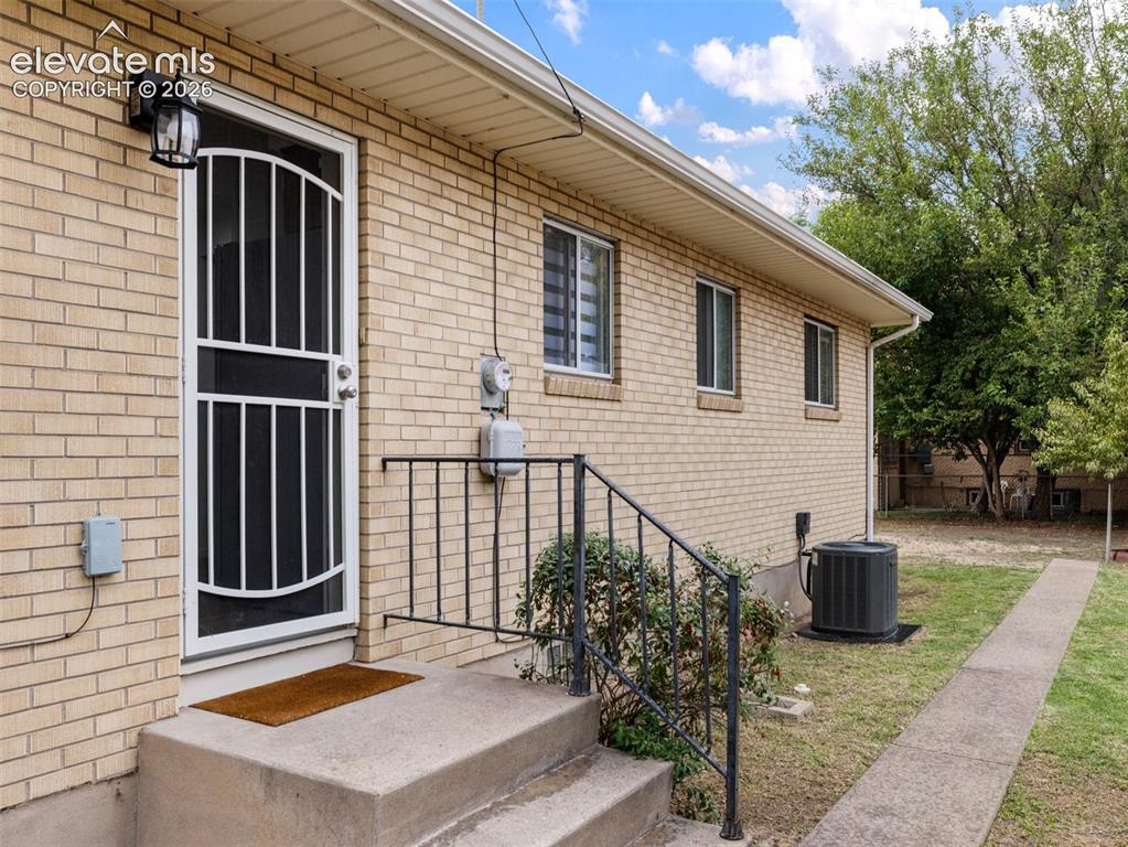 Image 27 of 34: Brick exterior with a security screen door, exterior lighting, concrete ste