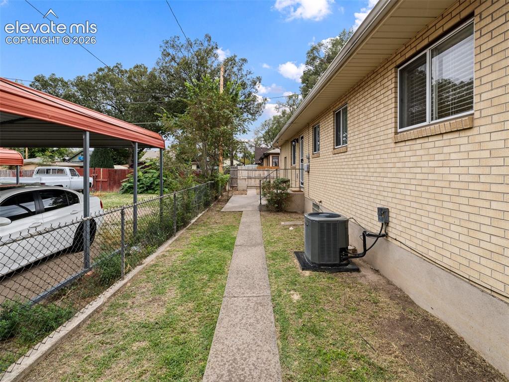 Image 28 of 34: Brick exterior with a concrete walkway, chain link fencing, and a red metal