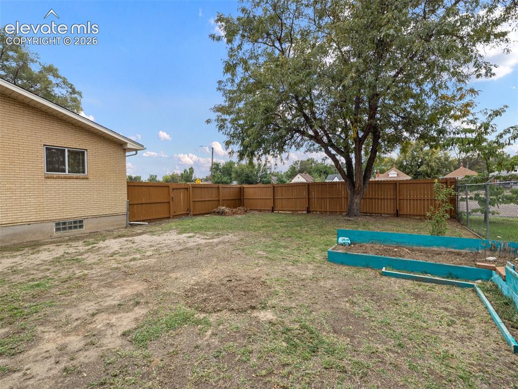 Image 30 of 34: Expansive backyard with a full privacy fence, mature shade tree, and raised
