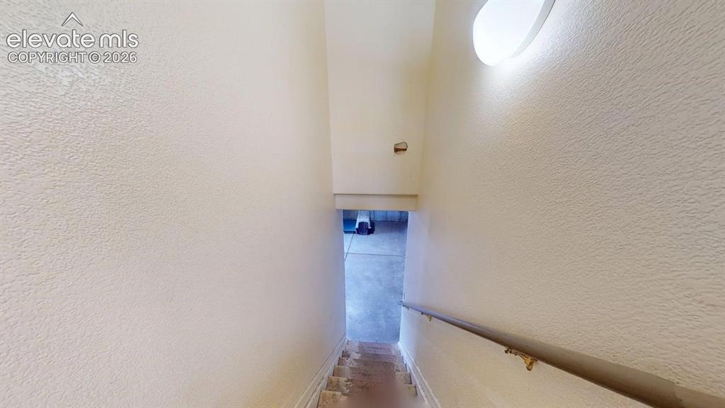 Image 16 of 20: Stairwell featuring a textured wall finish, a handrail, and an overhead flu