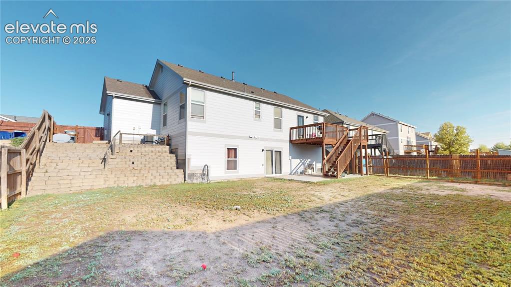 Image 2 of 17: Expansive backyard with a wooden fence, concrete patio, and elevated deck w