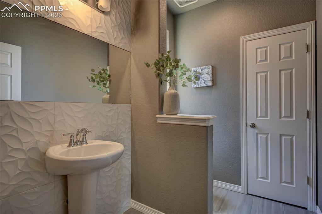 Image 25 of 50: Pedestal sink with chrome fixtures, set against a wall of textured dimensio