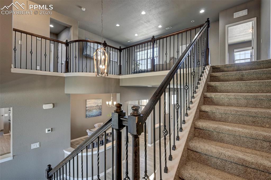 Image 26 of 50: Carpeted staircase with wrought iron balusters and dark wood handrails