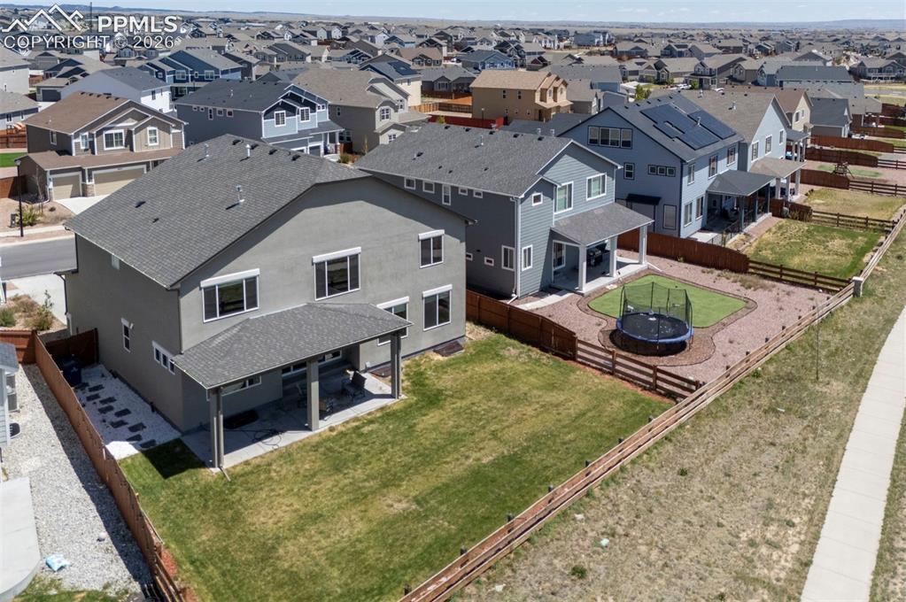 Image 49 of 50: Spacious backyard featuring a covered patio, extensive grass area, and ston