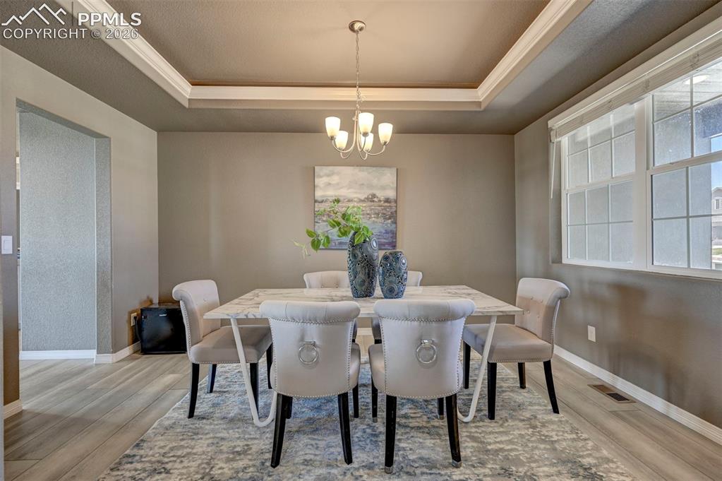 Image 8 of 50: Dining area featuring a tray ceiling, chandelier, wood-finish flooring, and
