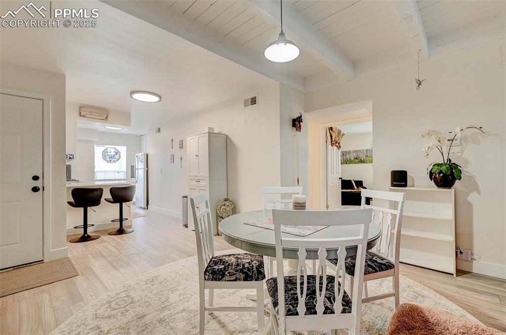 Image 2 of 16: Dining area with light wood-style floors and a wood ceiling with exposed be