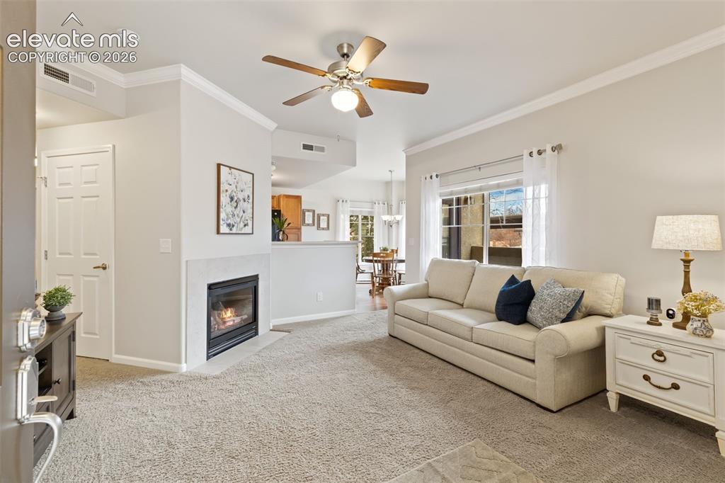 Image 2 of 31: Living area featuring a fireplace with a light-colored mantel, a ceiling fa