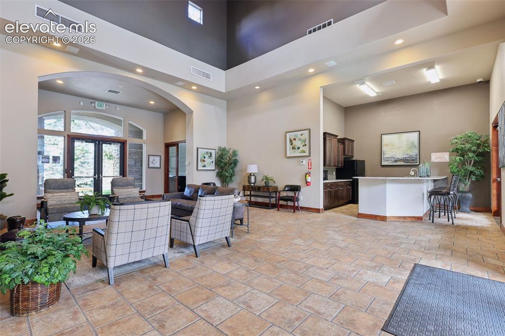 Image 24 of 31: Spacious common area featuring a stone fireplace, arched doorways, tiled fl