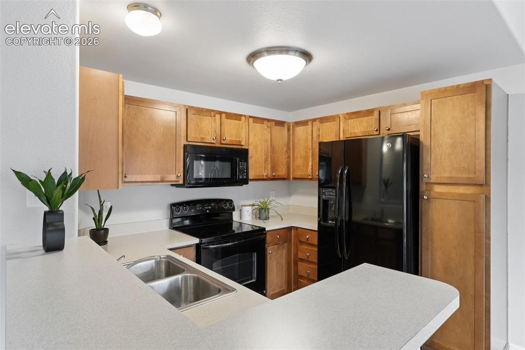 Image 7 of 31: Kitchen featuring wood cabinetry, black appliances, light countertops, and