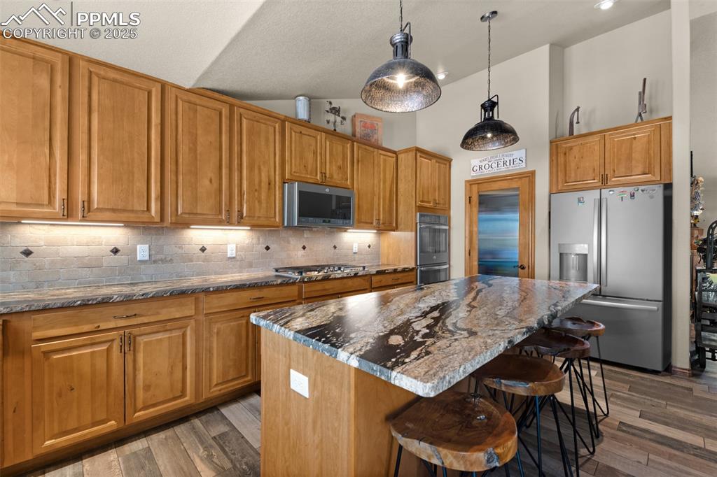 Image 12 of 48: Kitchen featuring stainless steel appliances, a kitchen bar, decorative bac