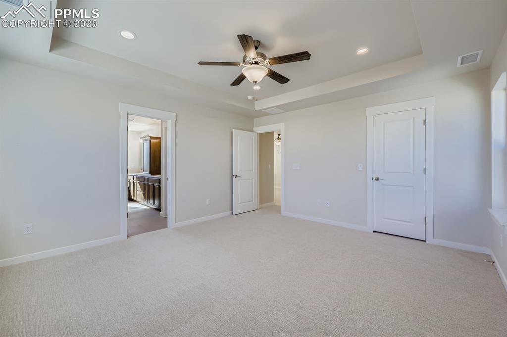 Image 12 of 27: Unfurnished bedroom featuring a raised ceiling, light carpet, ceiling fan, 