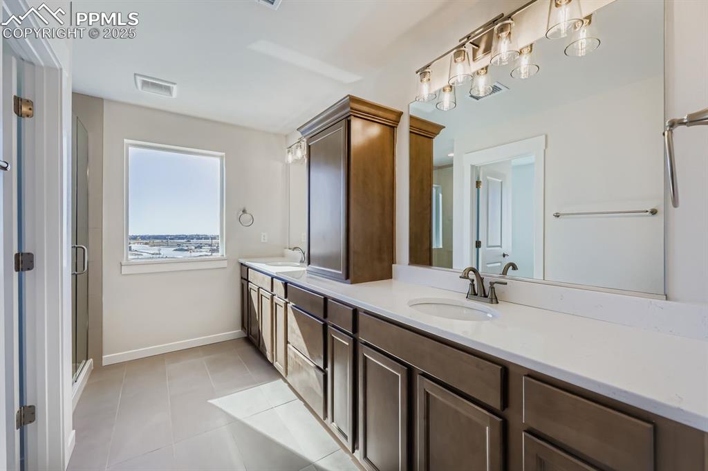 Image 13 of 27: Full bath featuring double vanity, light tile patterned floors, and a showe