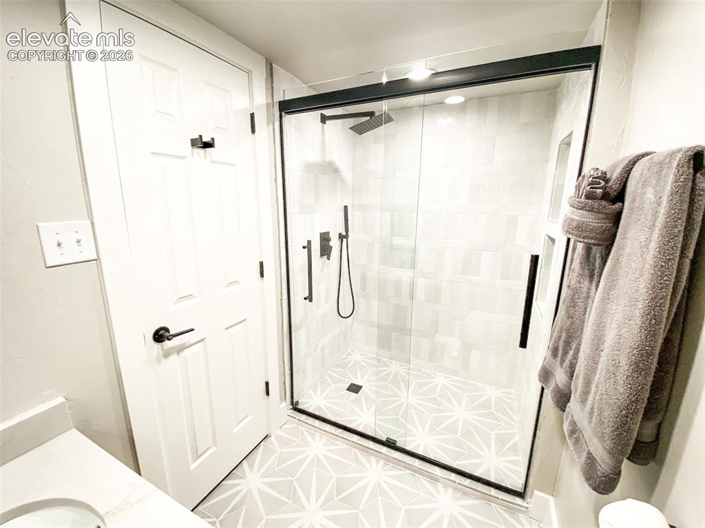 Image 10 of 29: Walk-in shower with geometric floor tile and rectangular wall tiles