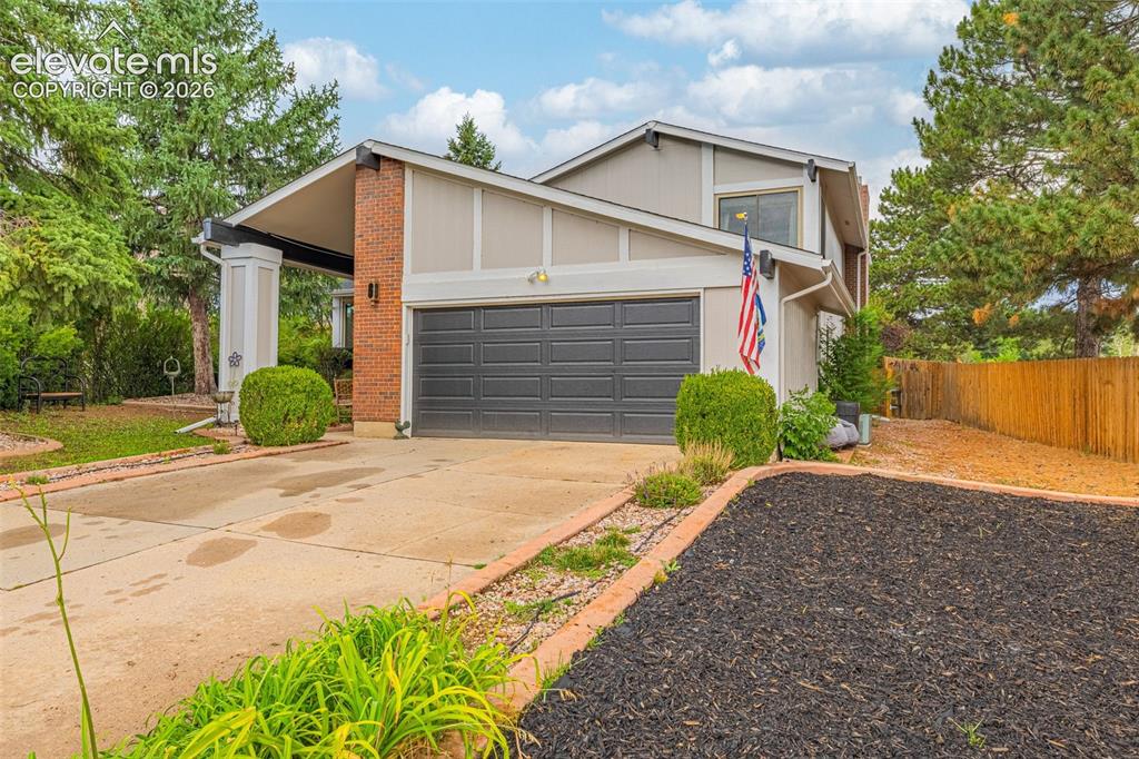 Caption: Front exterior featuring a multi-level design, attached garage, brick facade accents, and mature tre
