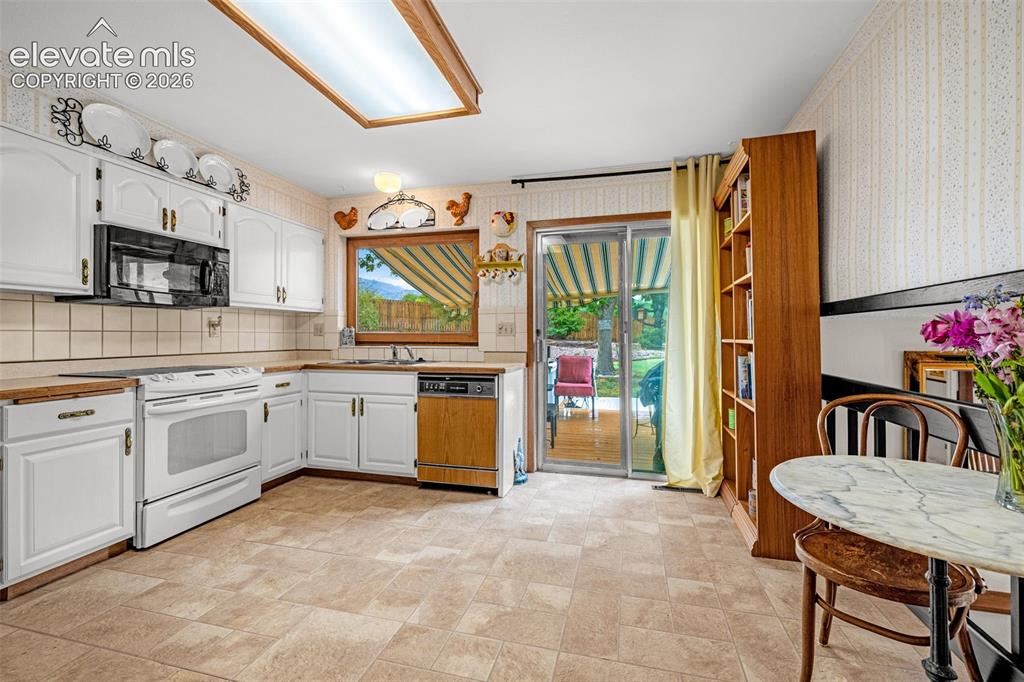 Image 11 of 45: Kitchen with white cabinetry, tile backsplash, built-in microwave, and wood
