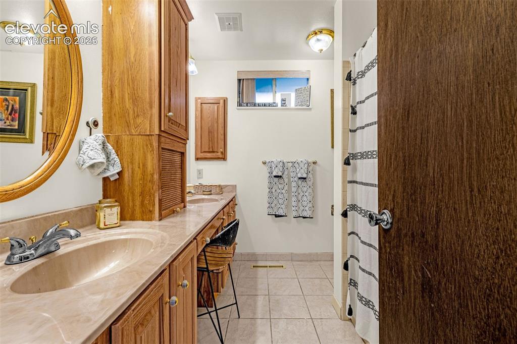 Image 18 of 45: Dual vanity with integrated sinks, ample wood cabinetry, and a full-height 