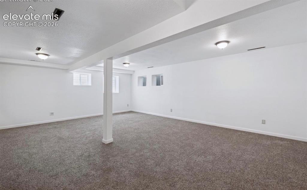 Image 32 of 45: Spacious finished area featuring gray carpeting, white painted walls, and c
