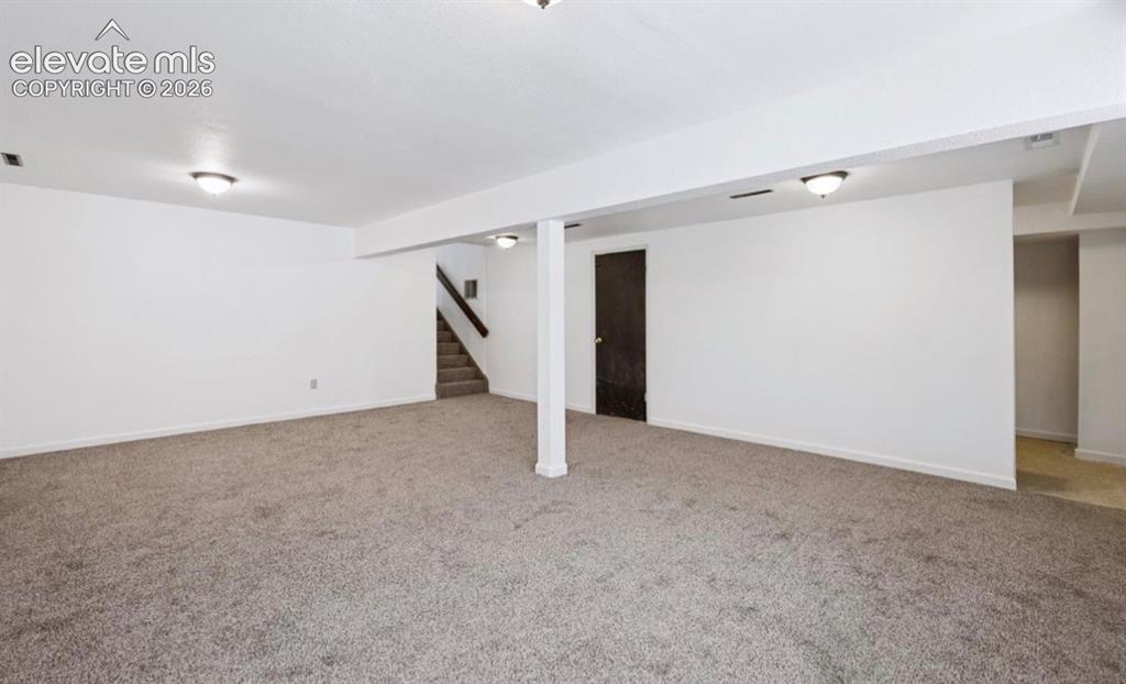 Image 34 of 45: Spacious room with plush gray carpeting, white walls, overhead lighting, an