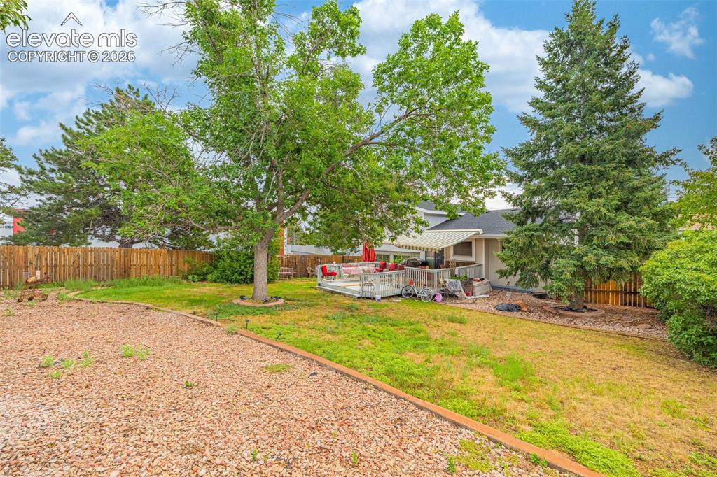 Image 39 of 45: Expansive backyard featuring a large deck with an awning, mature trees, a w