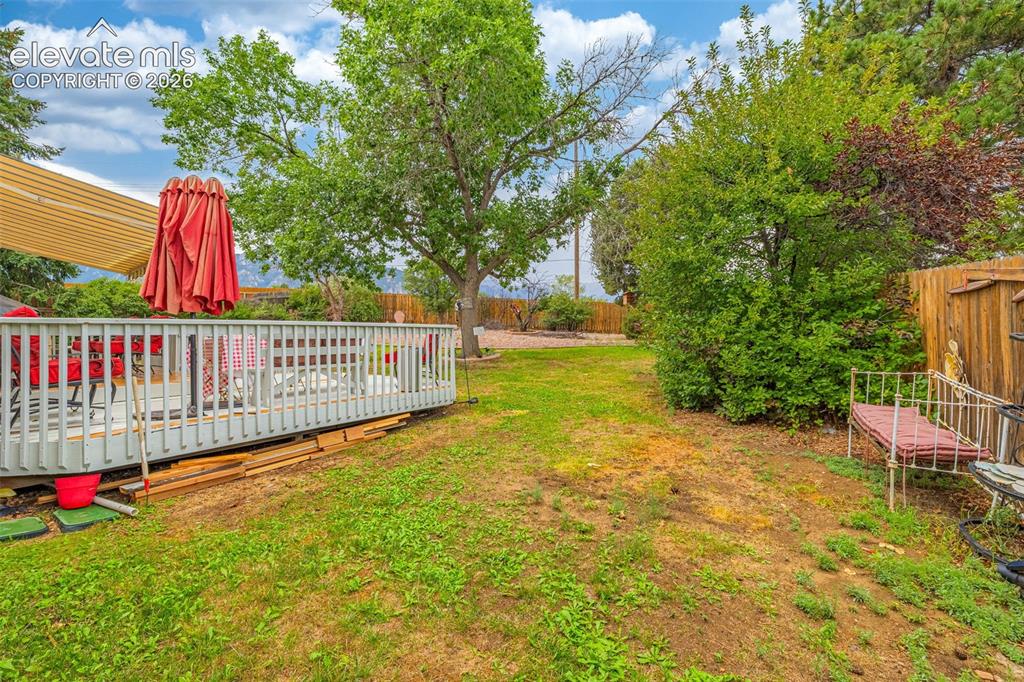 Image 40 of 45: Expansive green space featuring a large wooden deck with slatted railing an