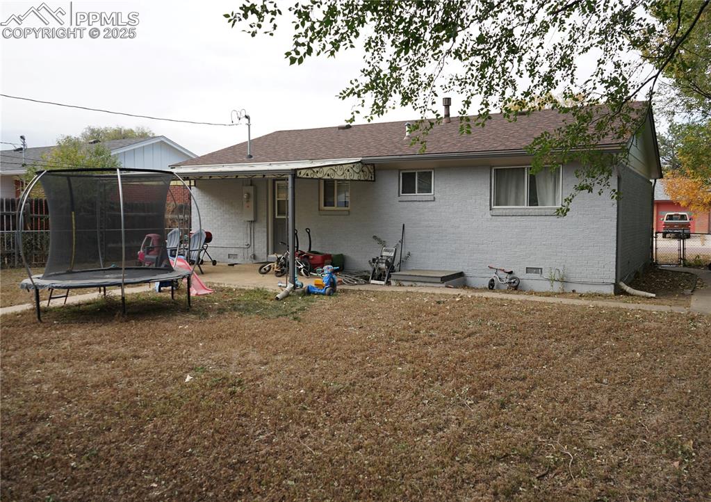 Image 17 of 22: Rear view of house featuring a trampoline, brick siding, a patio, a shingle