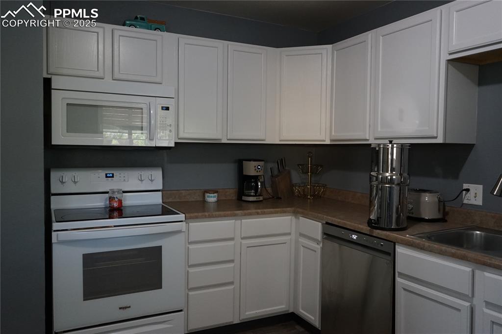 Image 4 of 22: Kitchen featuring white appliances, white cabinets, and dark countertops