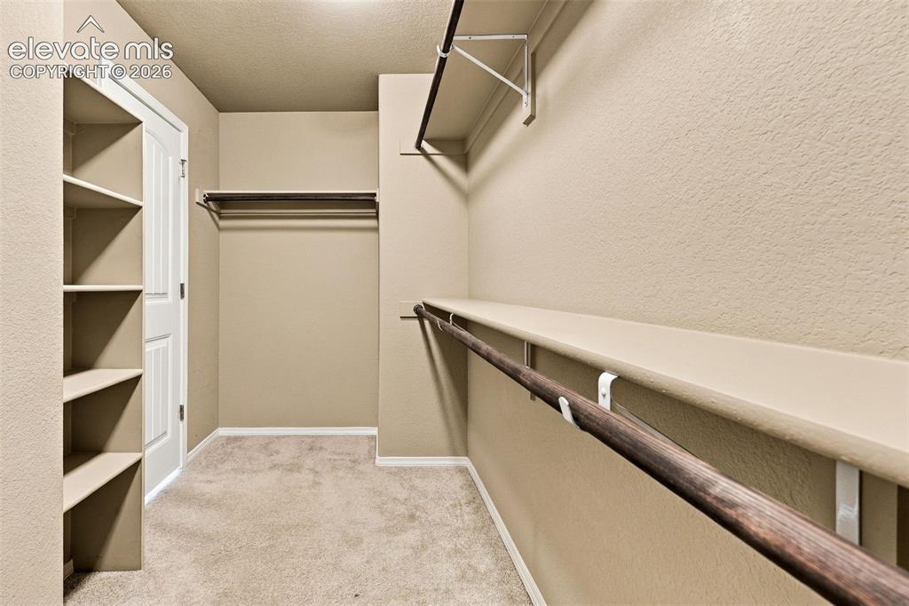 Image 30 of 49: Spacious primary walk-in closet with built-in shelving and hanging space.