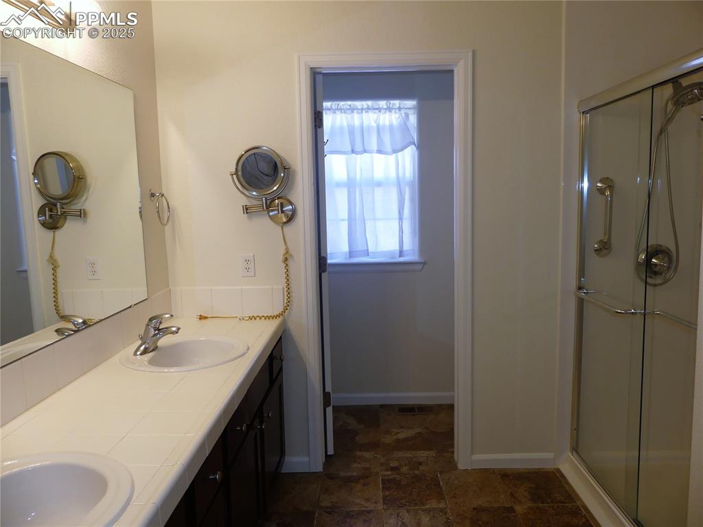 Image 17 of 33: Bathroom featuring double vanity, stone finish flooring, a sink, and a stal