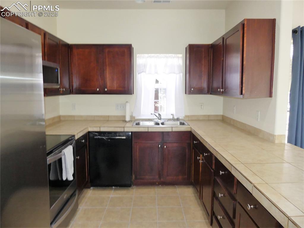 Image 8 of 33: Kitchen with a sink, stainless steel appliances, tile countertops, light ti