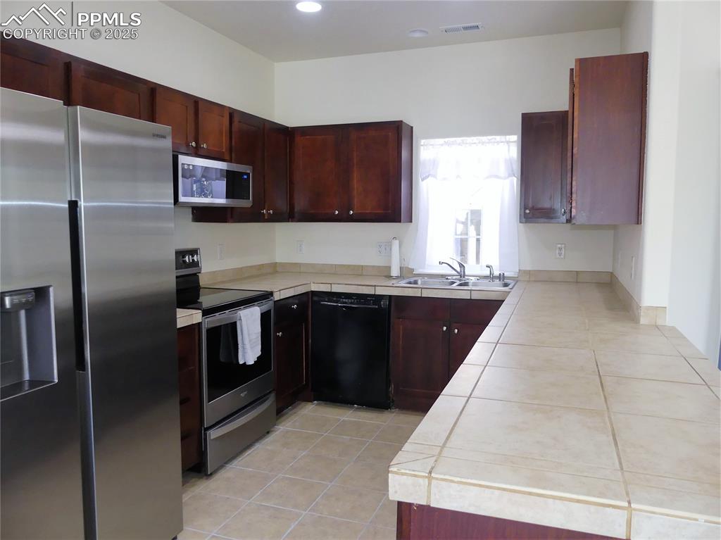 Image 9 of 33: Kitchen with light tile patterned flooring, reddish brown cabinets, a sink,