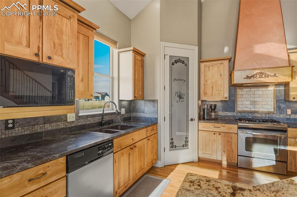 Image 17 of 49: Kitchen with stainless steel appliances, custom exhaust hood, backsplash, a