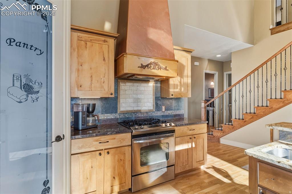 Image 18 of 49: Kitchen featuring gas stove, premium range hood, decorative backsplash, lig