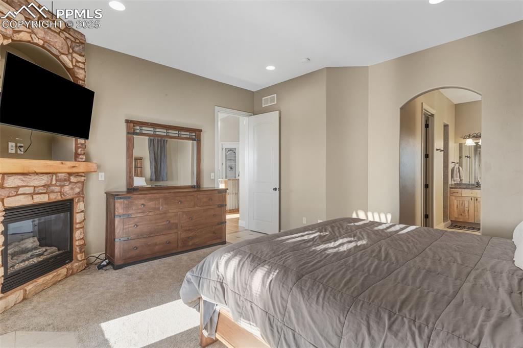 Image 24 of 49: Bedroom with a fireplace, arched walkways, carpet flooring, connected bathr