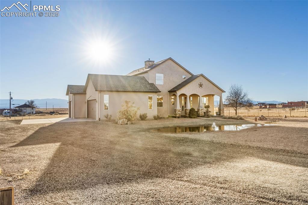 Image 44 of 49: View of front of home featuring stucco siding, driveway, a chimney, roof wi