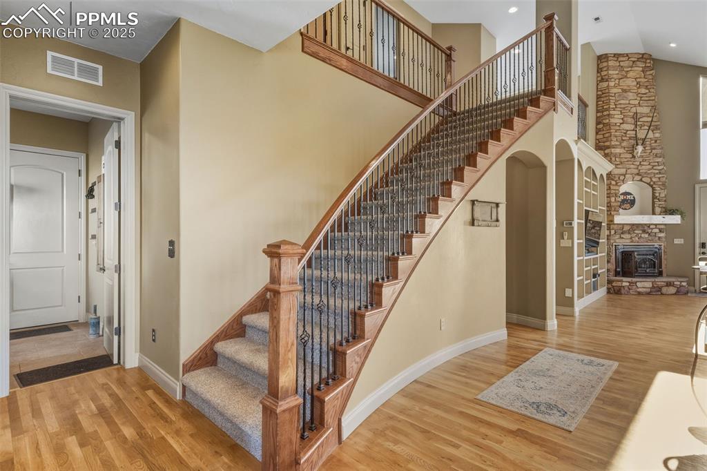 Image 8 of 49: Stairs with a high ceiling, wood finished floors, a fireplace, and arched w