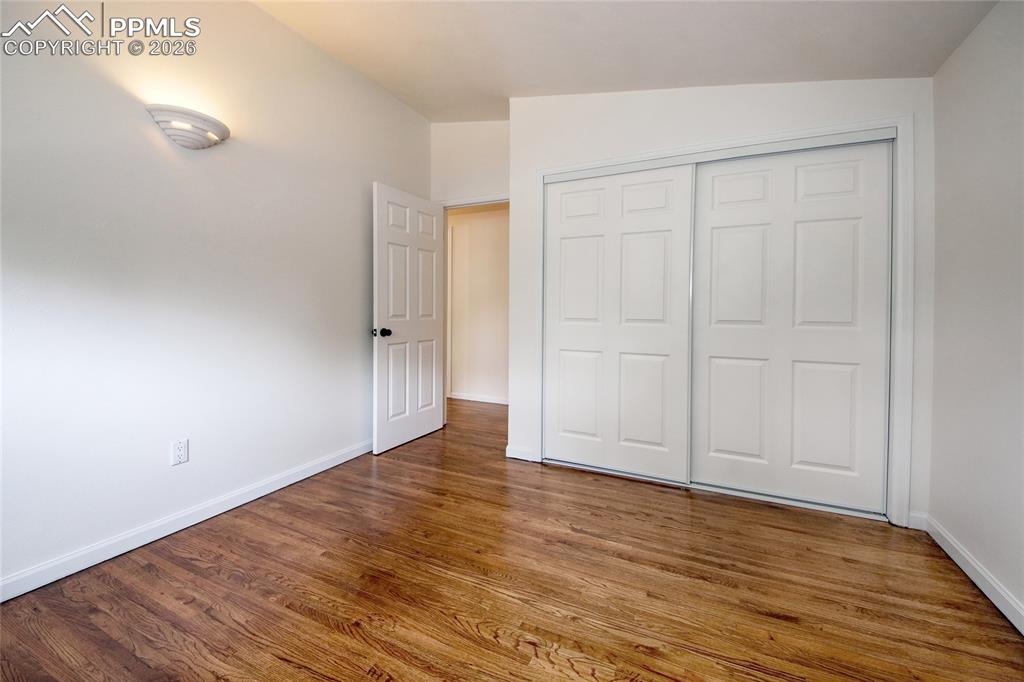 Image 17 of 27: Second bedroom featuring wood-finish flooring, white walls, and bright base