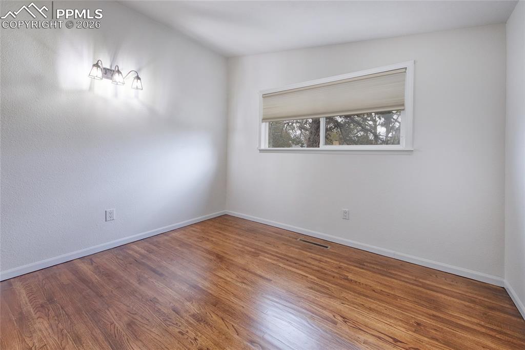 Image 18 of 27: Spacious third bedroom featuring wood-finish flooring, white walls, and a w