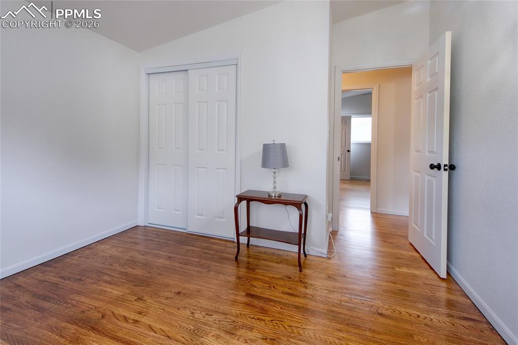Image 19 of 27: Bright third bedroom featuring wood flooring, white walls, vaulted ceiling,