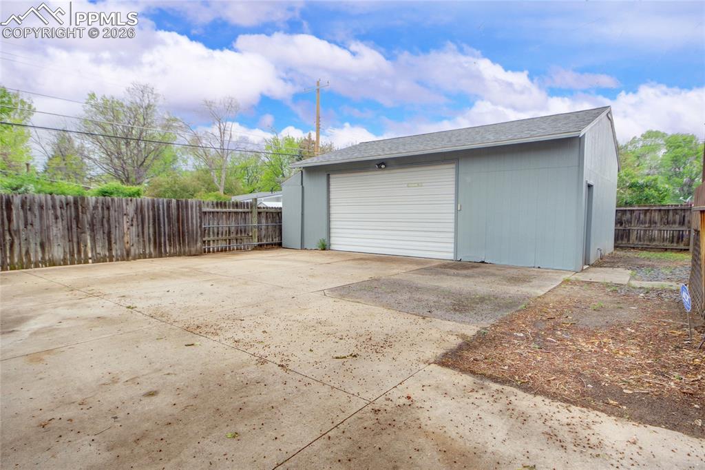 Image 25 of 27: Detached garage featuring light blue siding, a white roll-up door, and a si