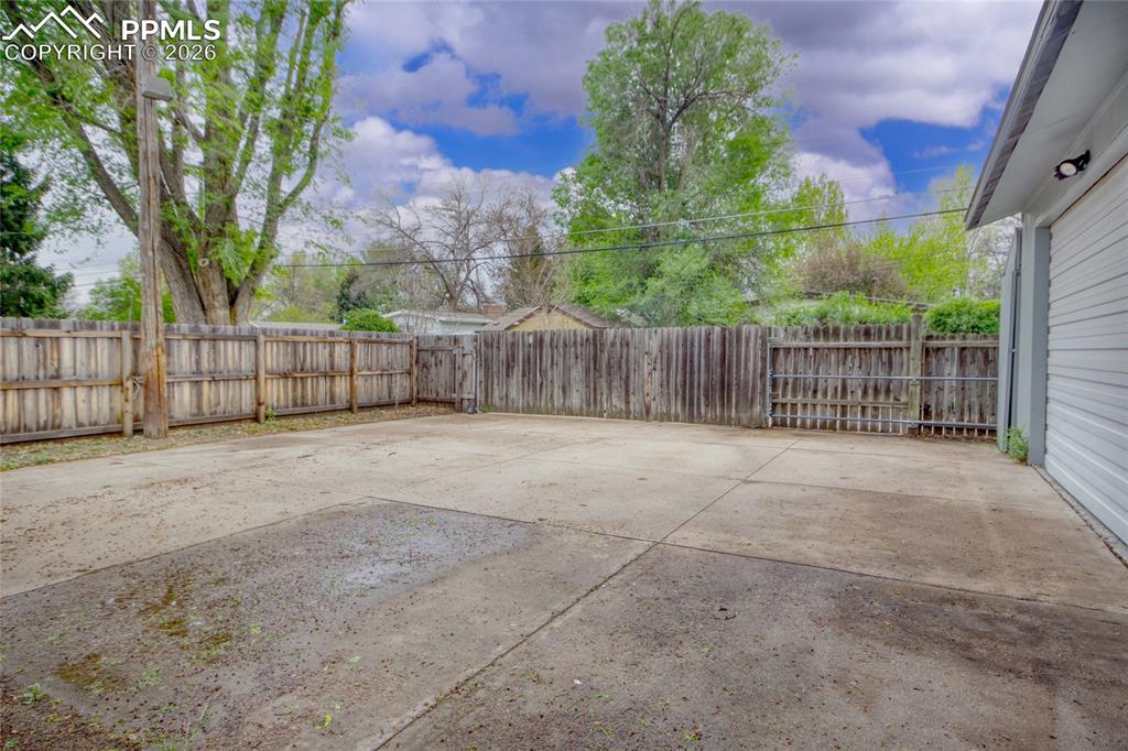 Image 27 of 27: Concrete patio area with a privacy fence perimeter and mature trees